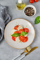 Caprese salad with sliced ​​tomatoes, mozzarella and basil on a plate on a light background