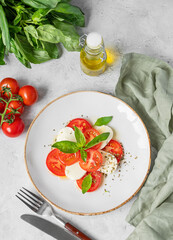 Fresh Caprese salad with tomatoes, mozzarella and basil on a plate on light background.