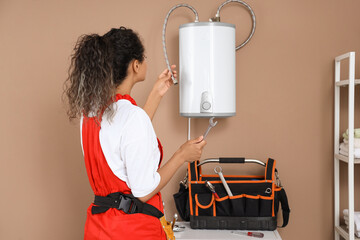 Female African-American plumber fixing boiler in bathroom, back view