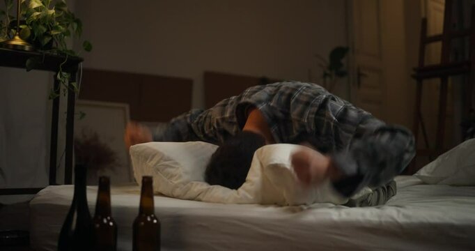 Man Falls Face Down On Pillow And Punches Up Mattress Lying On Mattress Near Empty Alcohol Bottles During Despair And Alcohol Addiction At Home
