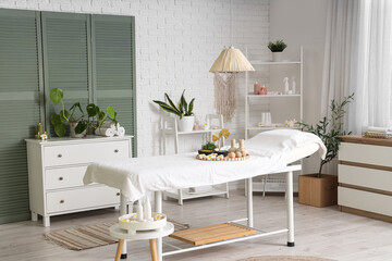 Interior of light spa salon with massage couch, shelf units and plants