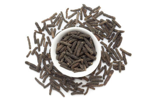 A bowl of Organic long pepper (Piper longum), placed over a heap of whole long pepper fruits. Isolated on a white background.