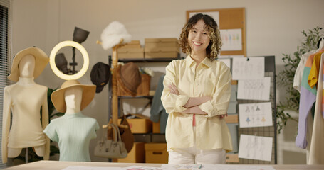 Portrait of Asian woman fashion designer looking at camera and positively smiling. Young female small business owner, tailor, dressmaker confidence with arms crossed. Successful people and workplace.