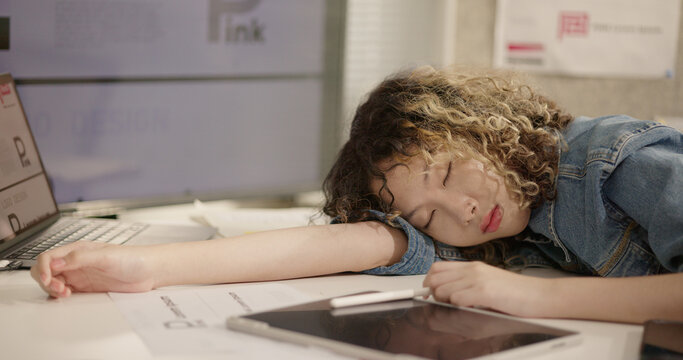 Exhausted young business woman graphic designer sleeping on desk after long hours of work. Overworked, tired and burnout female falls asleep at messy table with laptop after long workday. nap at work.