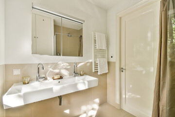 A clean and contemporary bathroom space featuring a sleek sink, large mirror, and cozy ambiance enhanced by natural light.