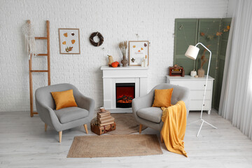Armchairs, fireplace with autumn decor in interior of living room