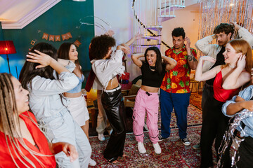 A multiracial group of friends dancing together indoors in a modern apartment living room, wearing colorful outfits and smiling during a lively party celebration.
