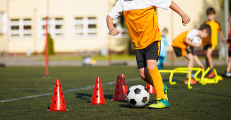 Obraz premium Football Boy in a Training Drill WIth Ball. Soccer Ball and Pylons on Turf Pitch. Youth Soccer Player Training. Young Footballer with Ball Training with Cones