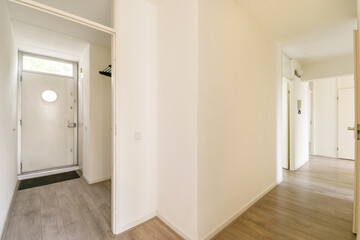 A bright, spacious indoor hallway featuring a simple design with clean lines, light-colored walls, and a doorway leading outside. Natural light enhances the inviting atmosphere.