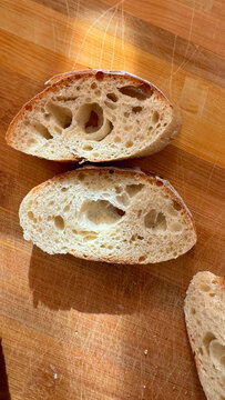 Two slices of sourdough bread with a light, airy crumb and large holes, resting on a wooden cutting board. Represents artisan baking and fresh bread