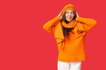Fototapeta premium Beautiful young Asian woman in knitted hat and scarf on red background
