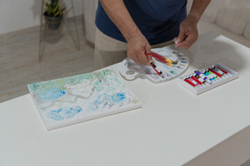 Senior man picking up paintbrushes while painting on canvas at home