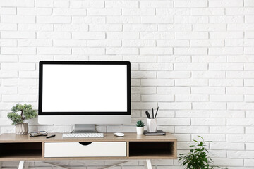 Fototapeta premium Stylish workplace with computer and stationery near white brick wall in light office