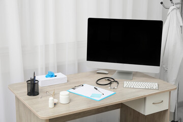 Doctor's workplace with blank computer monitor and medical supplies in office