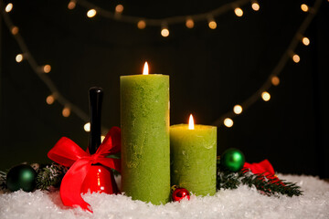Beautiful burning candles with Christmas decor on snow against dark background with lights