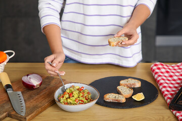 Young woman cooking vegan bruschetta at table in kitchen, closeup