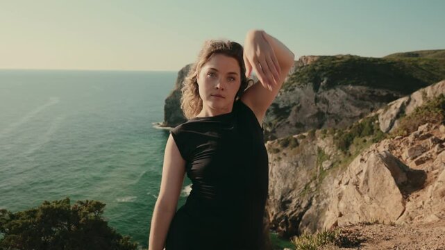 Woman in a dance pose on a cliffside with a breathtaking ocean view in the background. Captures freedom and expression.