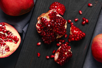 Wooden board with cut fresh pomegranate and seeds on black background, closeup