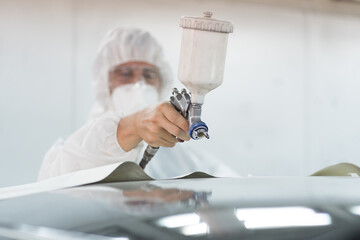Automotive paint services in car care workshop. Worker painting car with spray in chamber