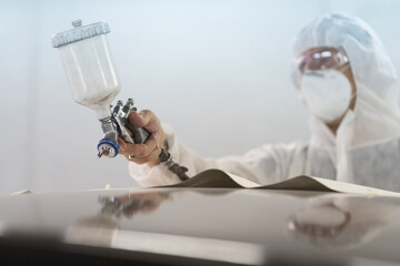 Automotive paint services in car care workshop. Worker painting car with spray in chamber