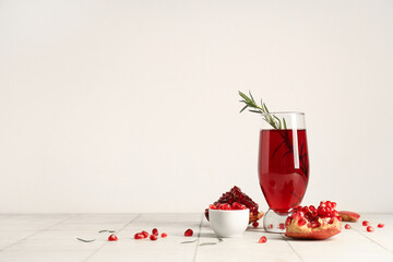 Glass of fresh pomegranate juice with rosemary and bowl of seeds on white tile table