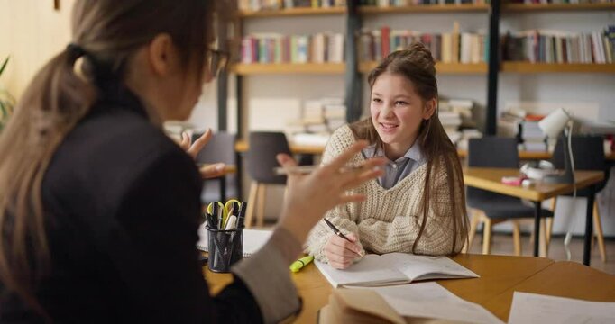 In a warm classroom filled with books, a student eagerly engages with her teacher while discussing school subjects and learning techniques in detail