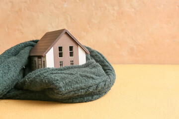 Model of house with warm scarf on beige background. Concept of heating season