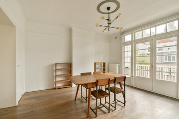 A stylish and minimalistic dining room featuring a wooden table and chairs, illuminated by natural light from large windows.