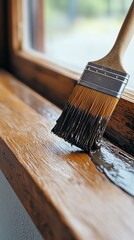 Close-up of paintbrush applying dark stain on wooden windowsill, home renovation concept, DIY interior woodwork detail