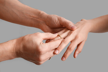 Man putting wedding ring on his woman's finger against grey background