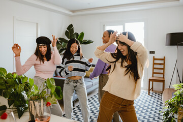 Four diverse women wearing casual clothes, Asian, White, and Latino dance and laugh together in a...