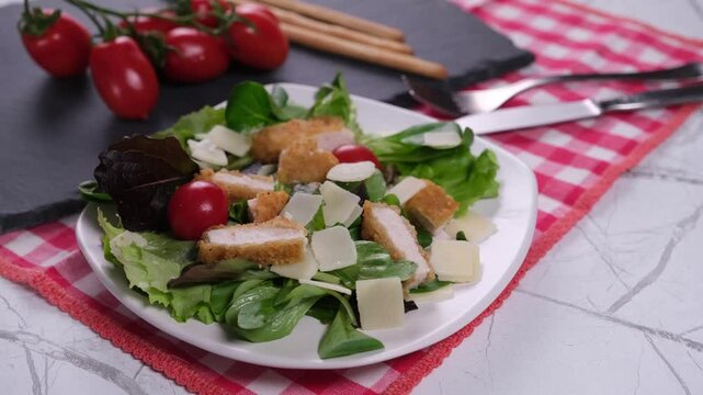 Insalata con pomodorini, scaglie di grana e pollo impanato, pomodorini in grappolo e grissini sul tagliere