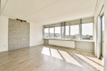 Spacious, bright room featuring large windows that allow sunlight to flood in, complemented by a stylish stone wall and wooden flooring.