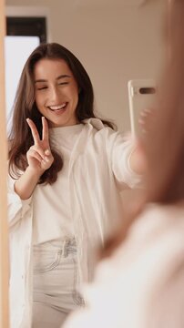 Radiant young woman captures herself on a smartphone, reflecting in the mirror with a joyful expression.