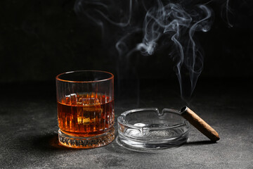Glass of cold rum and ash tray with cigar on grey grunge background
