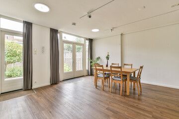 A spacious dining room with wooden furniture, large windows allowing natural light, and a minimalistic aesthetic. Ideal for family gatherings and intimate meals.