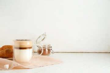 Glass cup of hot coffee and plate with tasty croissant on white background