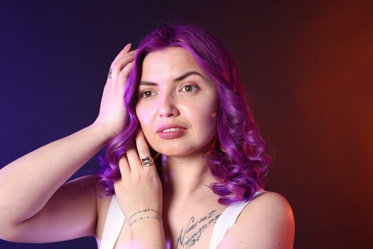 Beautiful woman with bright purple hair and tattoo in Latin on color background - Powered by Adobe