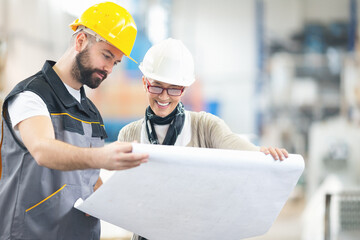 Engineers checking plans and smiling at factory