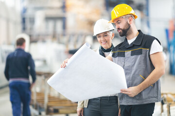 Senior female engineer checking blue prints with younger coworker inside a factory