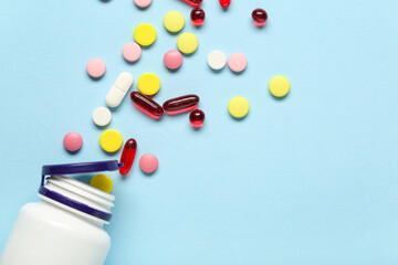 Bottle with scattered pills on blue background, closeup