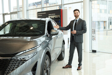 Happy salesman near new grey car in salon