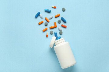 Bottle with scattered pills on blue background