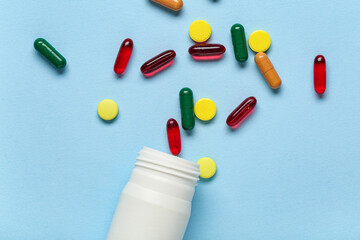 Bottle with different scattered pills on blue background, closeup