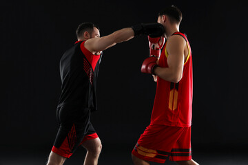 Men in boxing gloves fighting on black background