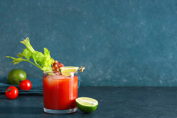 Glass of bloody mary cocktail with bacon, celery and lime on blue background