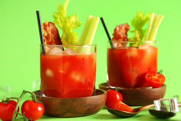 Glasses of bloody mary cocktail with bacon and celery on green background