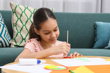 Girl applying glue onto paper figure for her creative project at table indoors. Art and craft