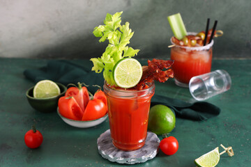 Glasses of bloody mary cocktail with bacon, celery and lime on green table