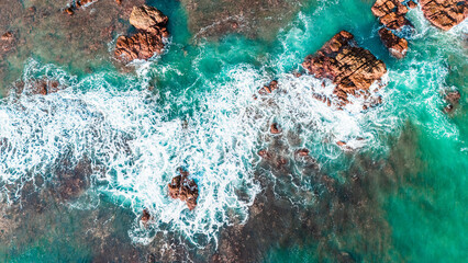 Rocky cliff coast and breaking waves top-down drone photo with summer beach vibes.